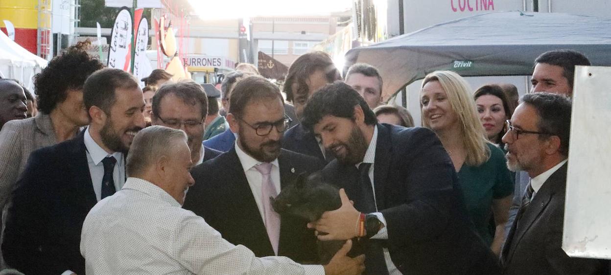 El presidente de Murcia coge un lechón de chato murciano ante el alcalde y el delegado, ayer. 