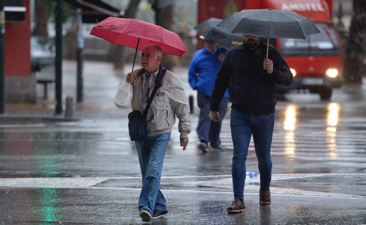 Tres hombres caminan bajo la lluvia con un paraguas, en una foto de archivo.
