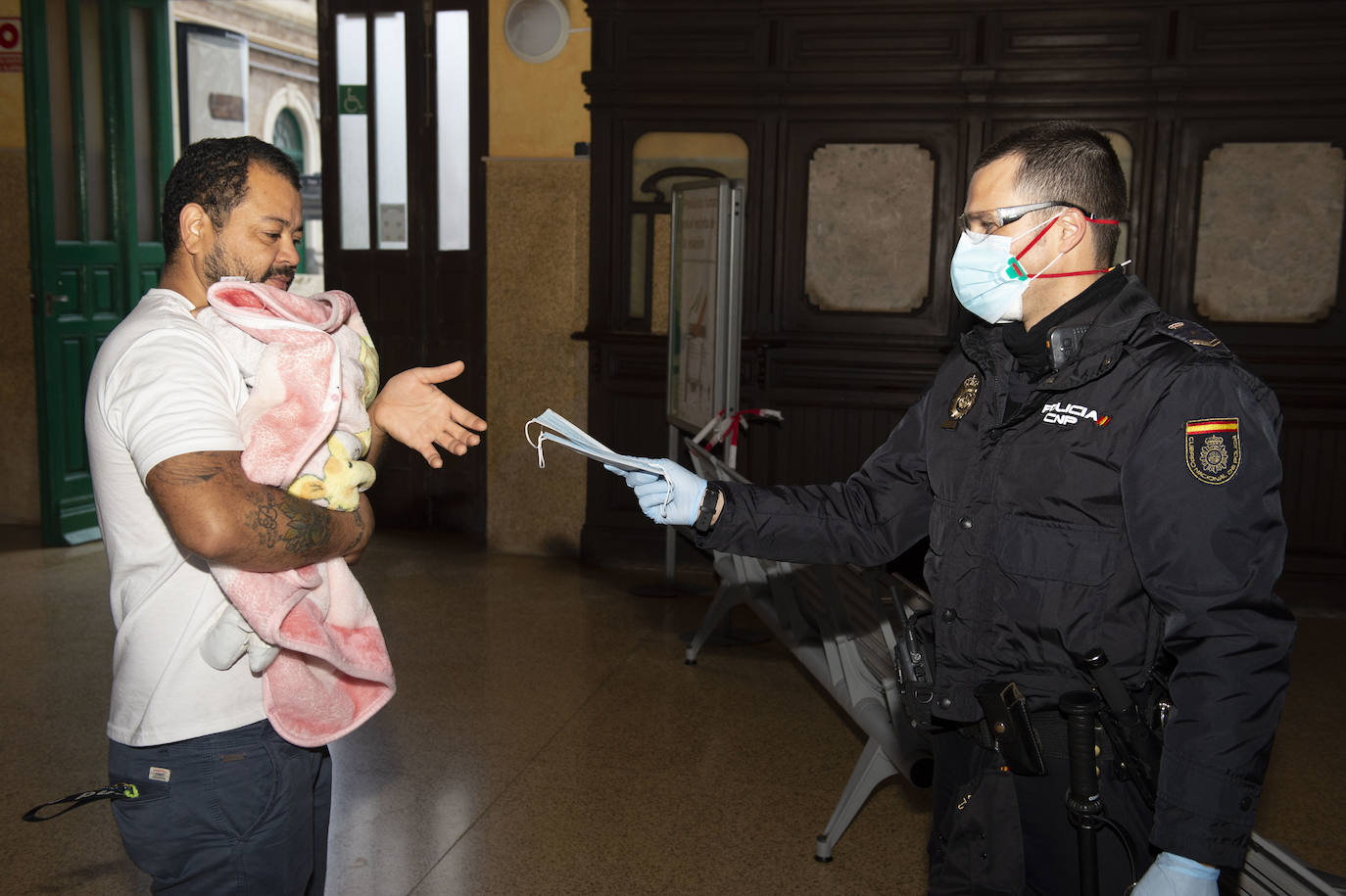 Un agente de Policía Nacional da una mascarilla a un ciudadano en la estación de tren de Cartagena.