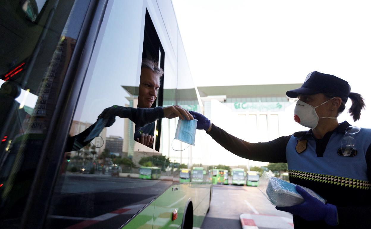 Una agente da una mascarilla a un conductor de autobús. 