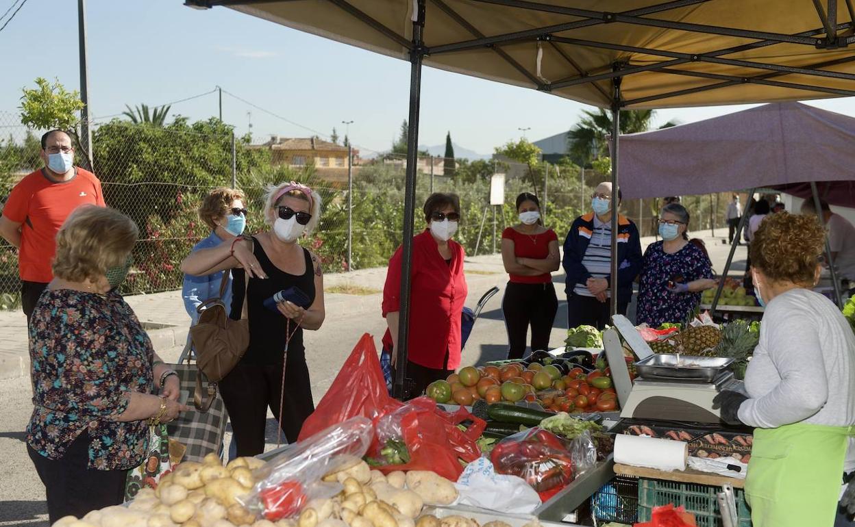 Varias personas esperan a ser atendidas en un puesto de verduras del mercadillo de Algezares, este lunes.