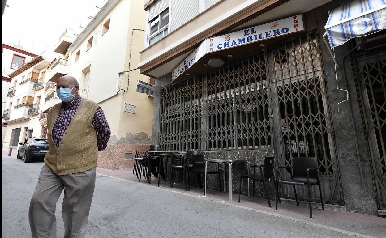 Un vecino de Abanilla, protegido por una mascarilla, caminando este martes por la tarde frente a uno de los bares de la localidad, con sus puertas cerradas.