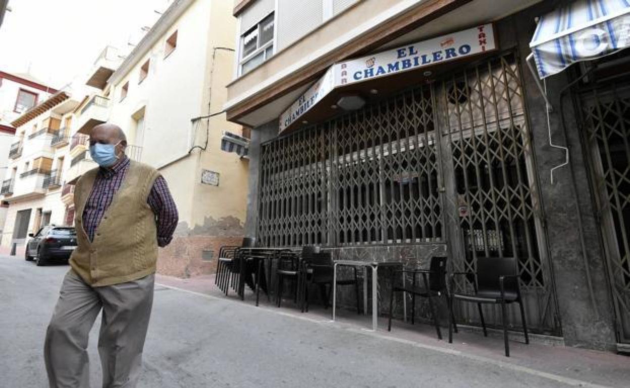 Un vecino de Abanilla, protegido por una mascarilla, frente a uno de los bares de la localidad, con sus puertas cerradas.