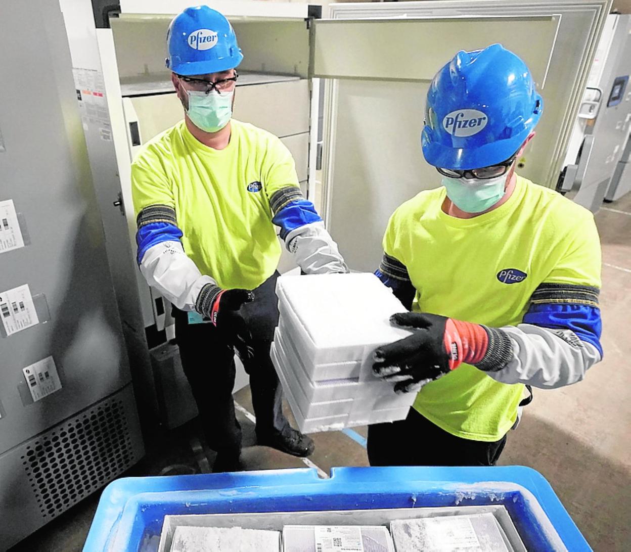 Dos trabajadores de un centro de producción de la multinacional farmacéutica Pfizer llenan una caja con dosis de vacunas. 