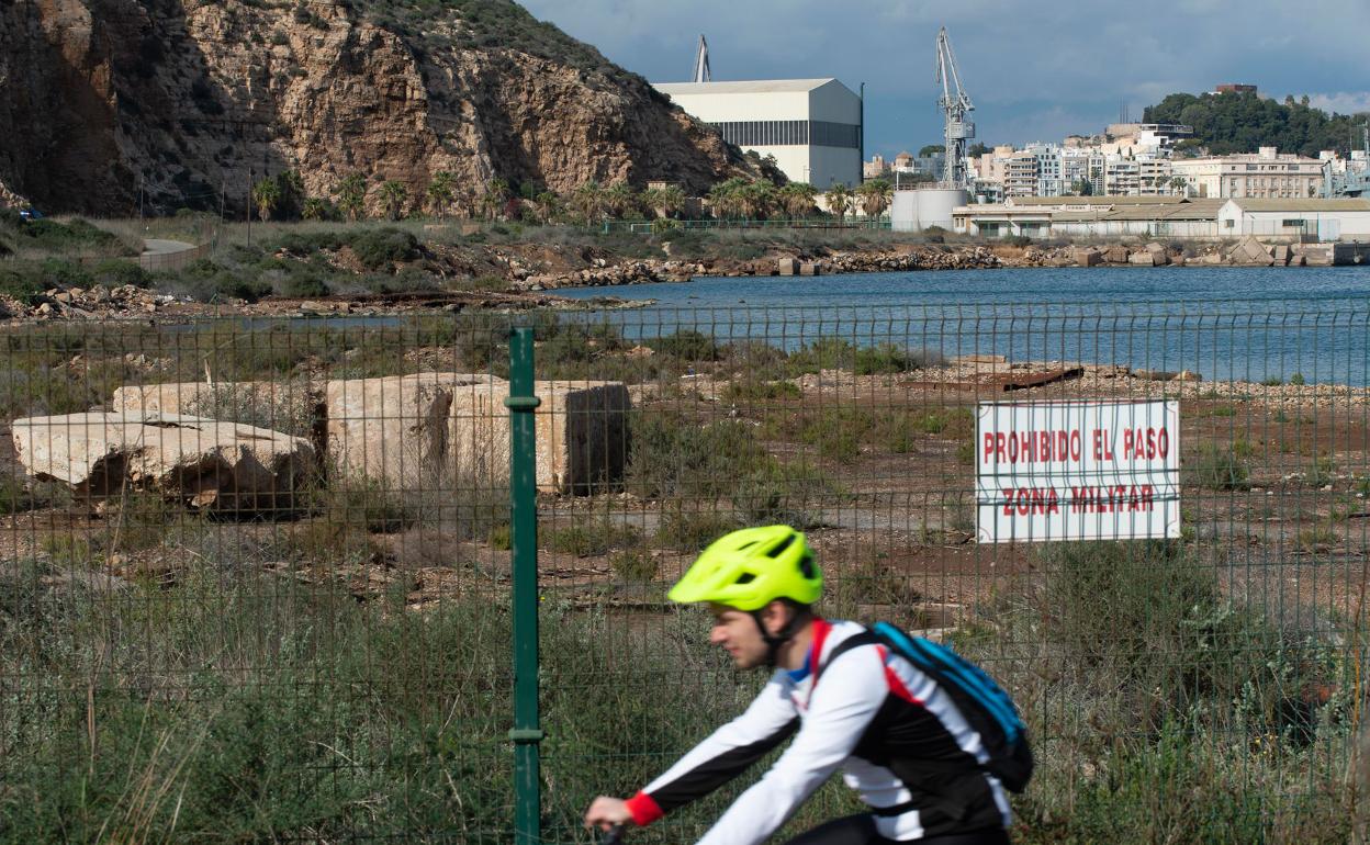 Un ciclista transita por la carretera del faro de Navidad, con los terrenos del Espalmador y el Muelle del Carbón de fondo.