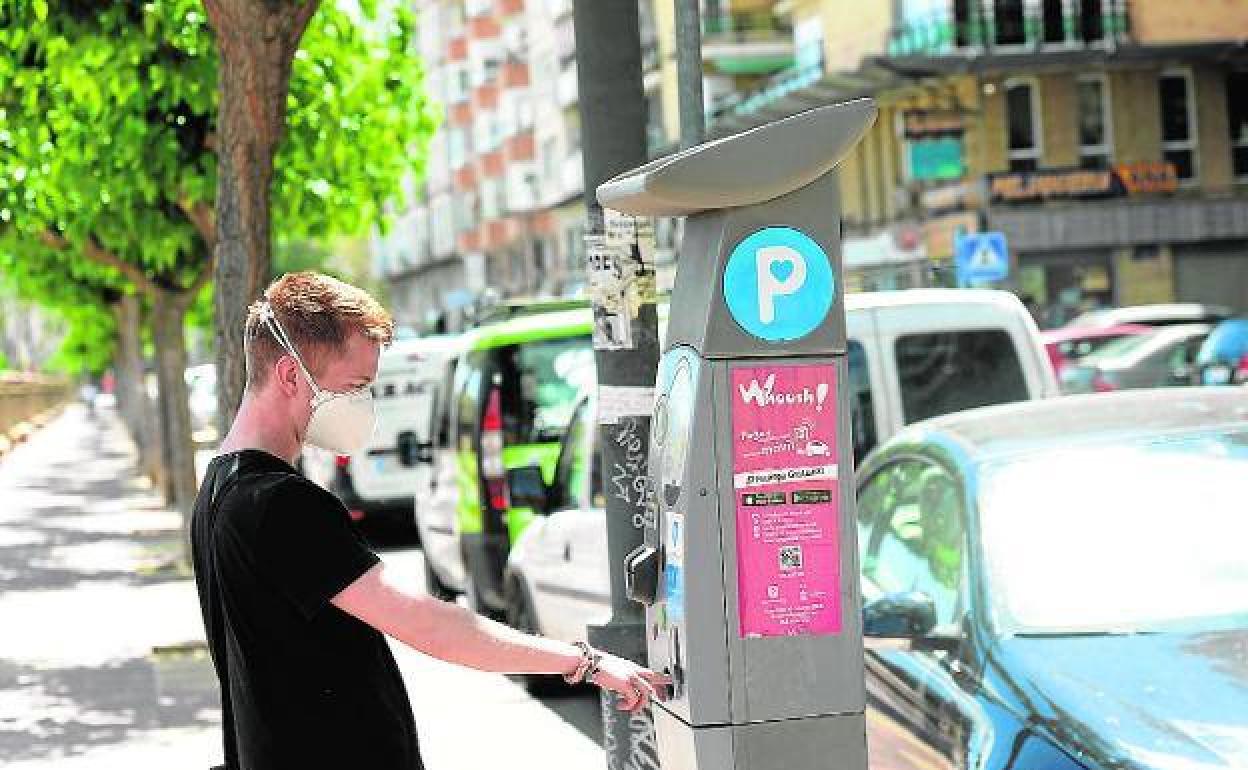 Un joven introduce monedas en un parquímetro para obtener su correspondiente tique.