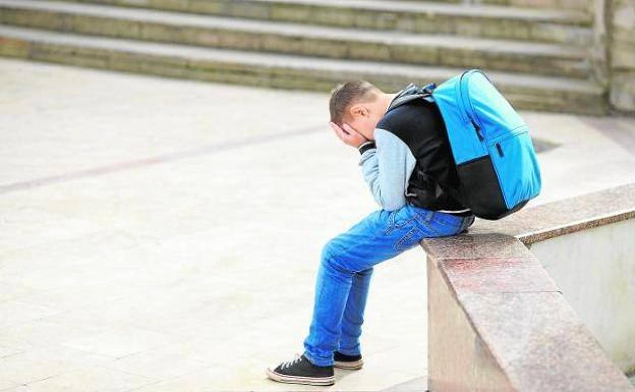 Un escolar sentado en la calle con la cara cubierta. 