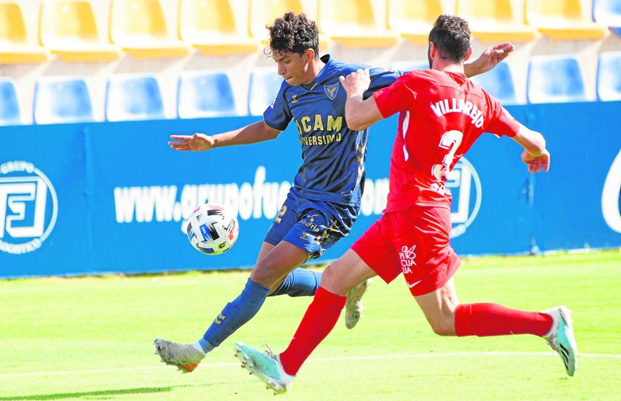 Johan intenta golpear el balón con Villarejo tapándolo, en un enfrentamiento entre UCAM y Linares, dos equipos de la Primera RFEF. 