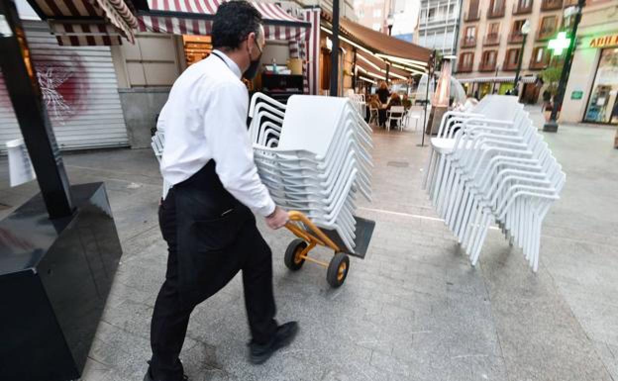 Un hostelero transporta las sillas de una terraza. 