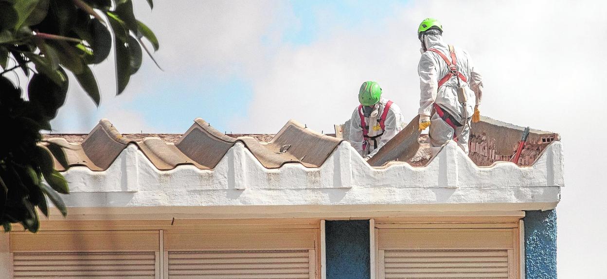 Dos trabajadores ataviados con trajes de seguridad, trabajando en la retirada de la cubierta del colegio Virgen del Carmen, ubicado junto a la Asamblea Regional. 