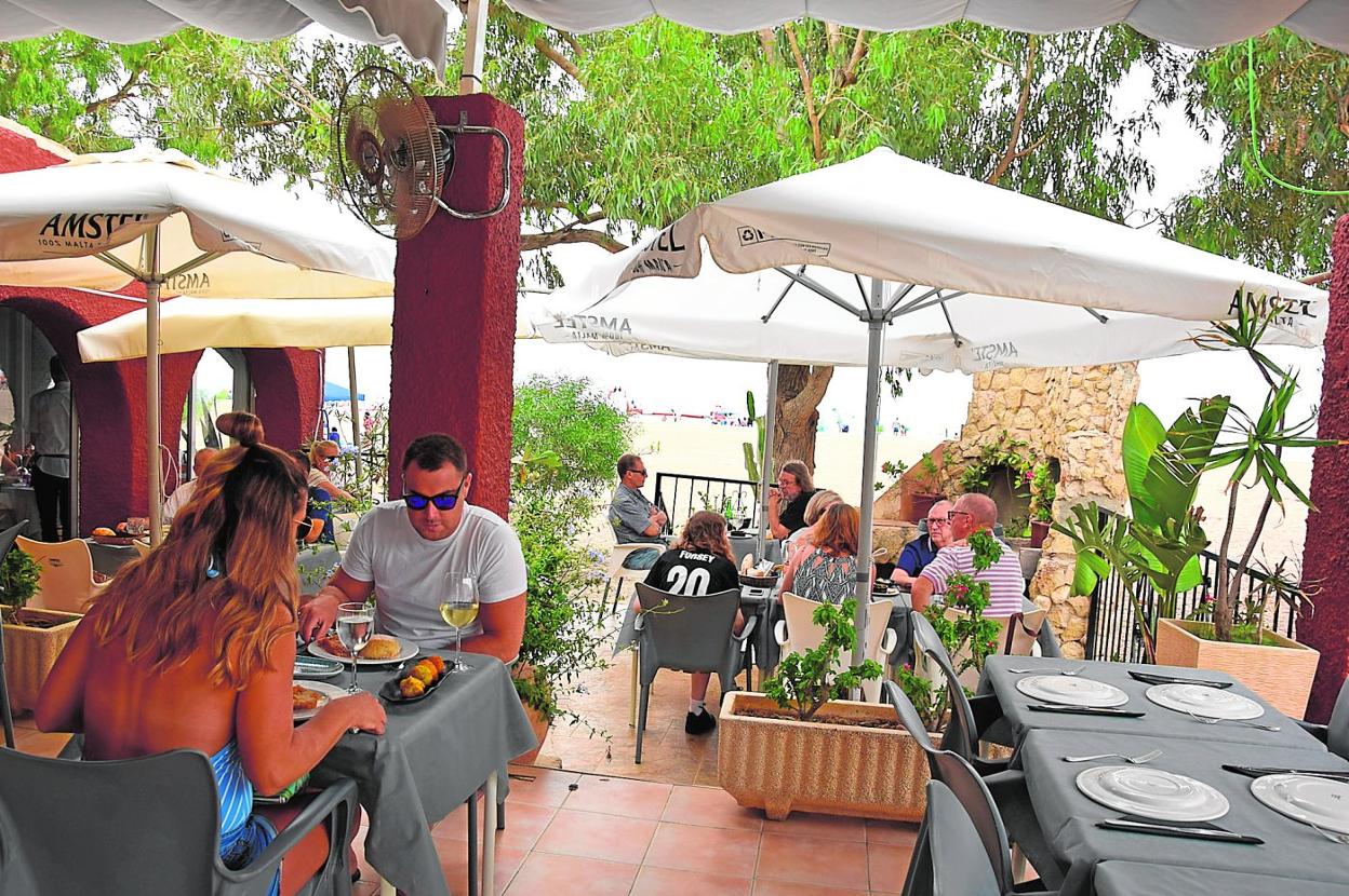La terraza de La Siesta, en la playa de Bolnuevo. En detalle, el hostelero Oliver Gómez sirviendo unas croquetas caseras en la terraza cubierta. 