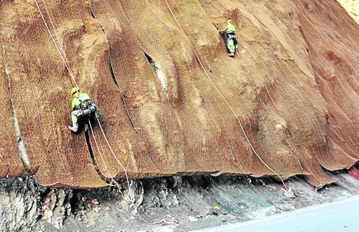 Dos operarios refuerzan uno de los taludes de la carretera. 