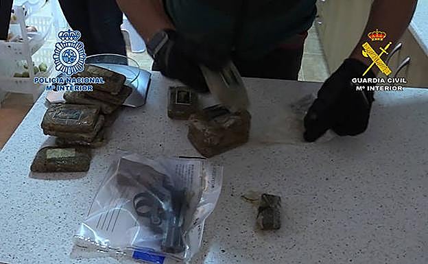 Un agente manipula varias cantidades de droga y un arma de fuego.