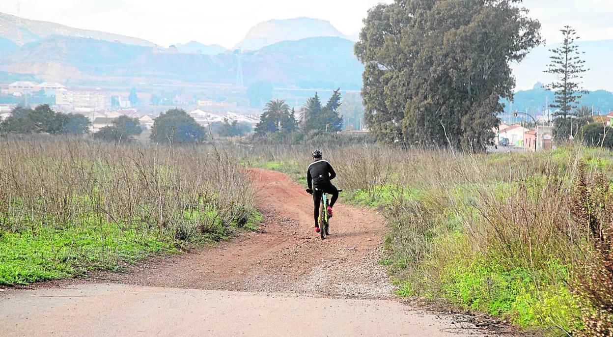 Un ciclista se adentra por el tramo del camino que está sin asfaltar y por donde iría la vía de evacuación, con el pueblo de Alumbres al fondo. 