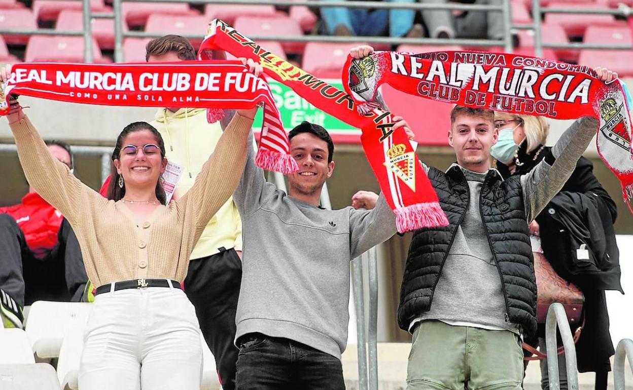 Tres aficionados del Real Murcia muestran su bufanda en un partido del equipo.