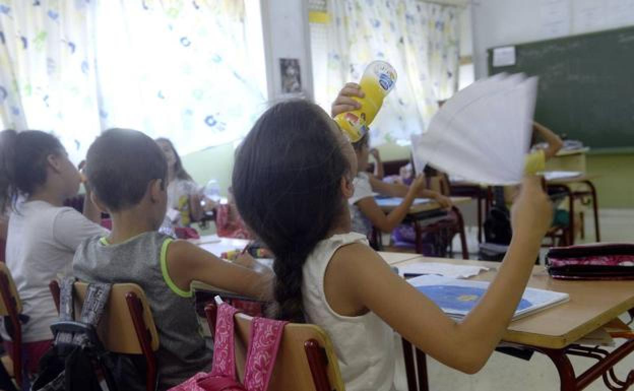 Una niña se abanica y bebe agua durante una clase en el colegio Ciudad de La Paz de El Palmar. 