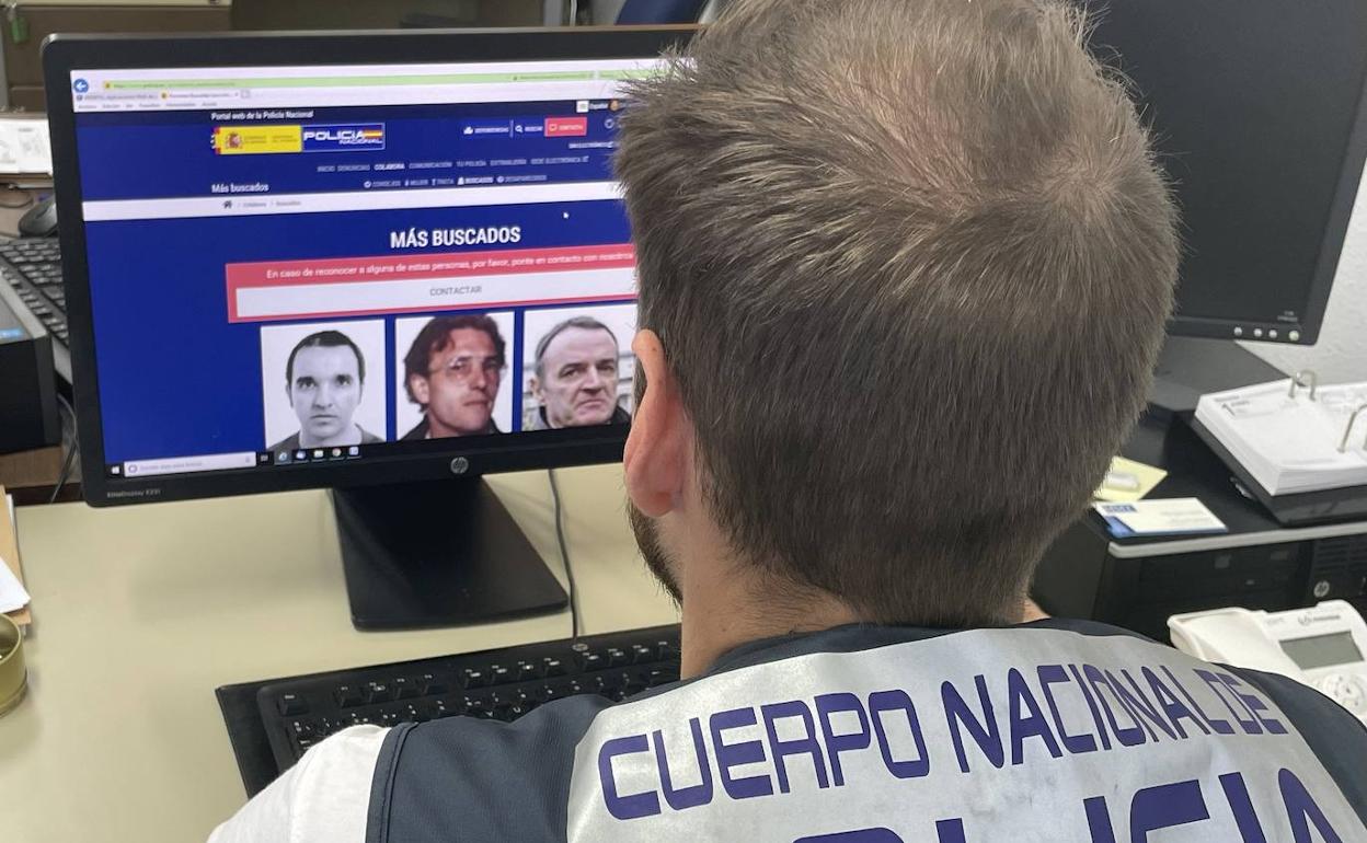 Agente de la Policía Nacional frente a la página web de los más buscados.