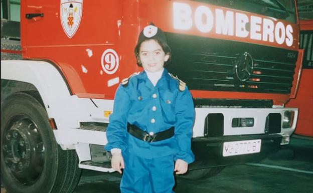 Irene con 7 años vestida de bombero delante de un camión. 