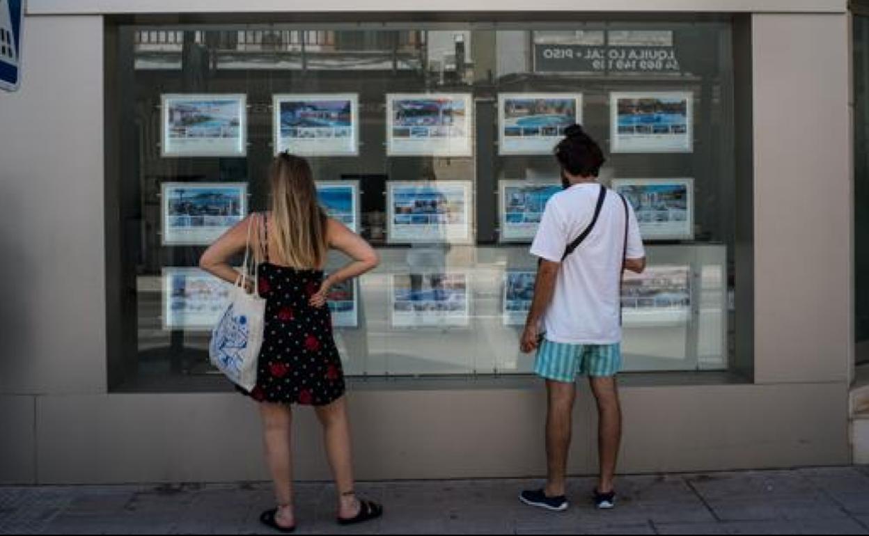 Dos jóvenes buscan una vivienda de alquiler en una inmobiliaria.