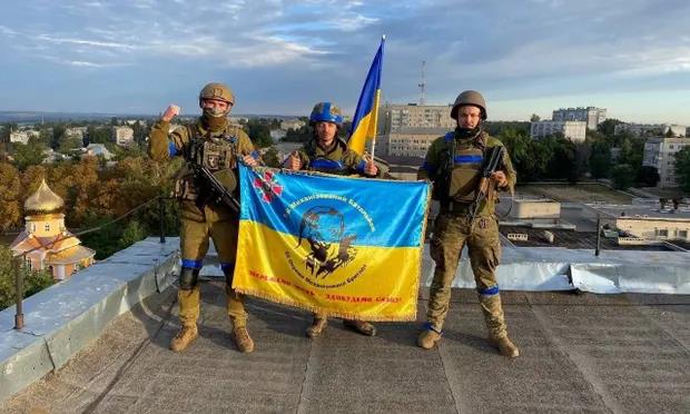 Tres soldados ucranianos muestran su bandera en una azotea de la reconquistada Kupiansk