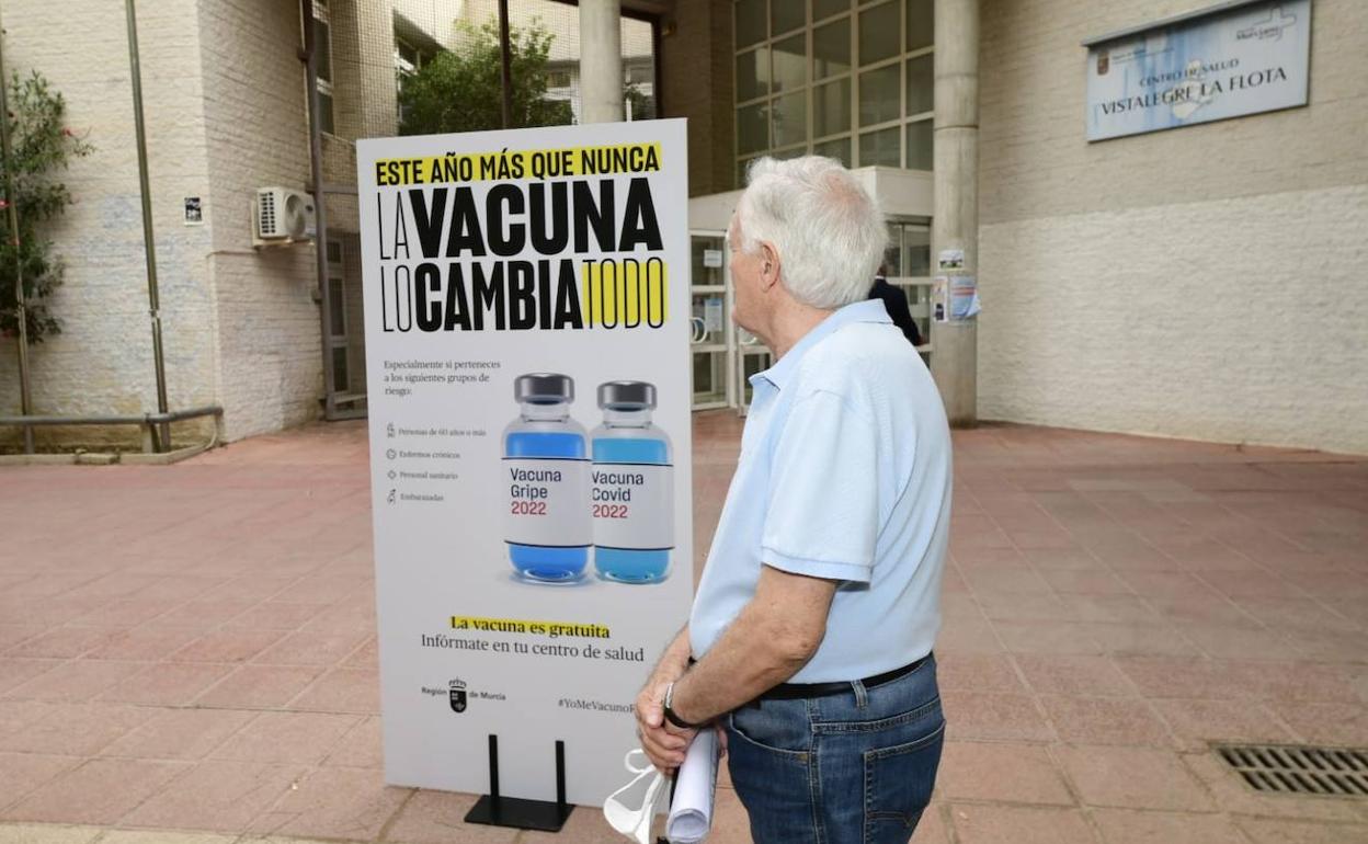 Un hombre, a las puertas de un centro de salud junto a un cartel para promover la vacunación.