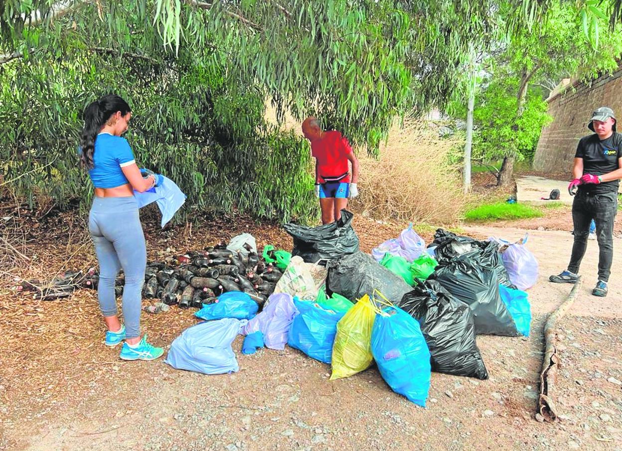Tres voluntarios junto a las botellas de cristal y la bolsas de basura recogidas hace tres fines de semana. 