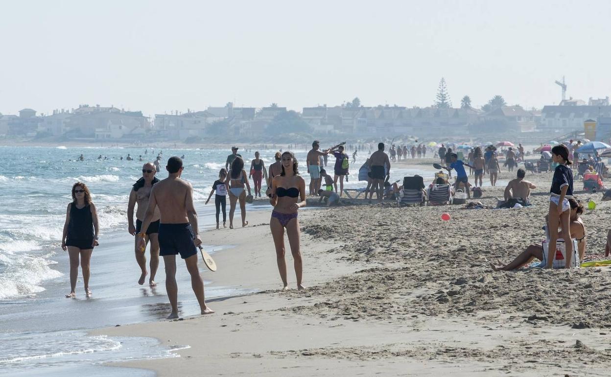Una playa de La Manga del Mar Menor, con personas tomando el sol y bañándose en el mar en la mañana de ayer. 