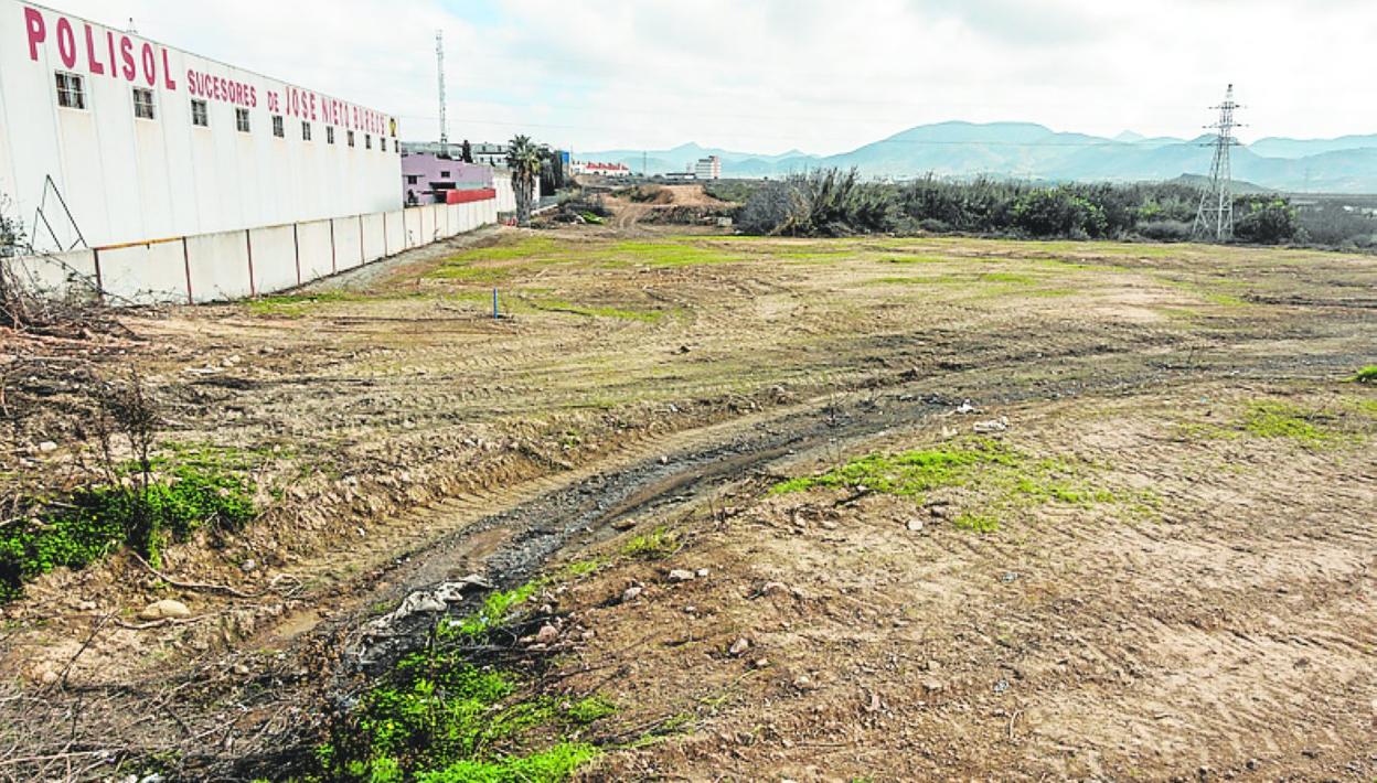 Terrenos roturados y desbrozados, junto a una nave industrial. 