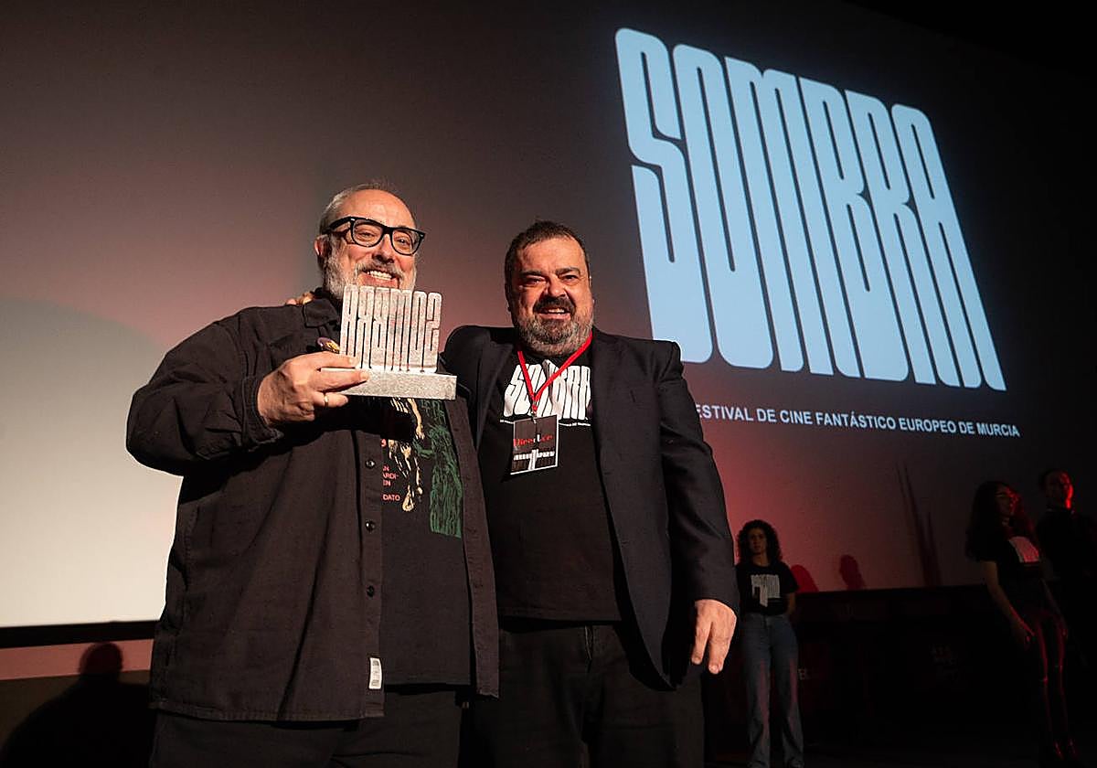 Álex de la Iglesia muestra sonriente el galardón junto al director del festival, Javier García.