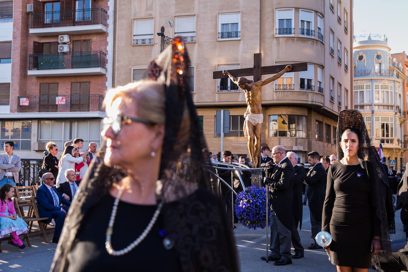 La imagen del Cristo de las Santas Mujeres atraviesa el Puente Viejo. En primer plano, una mujer de mantilla.
