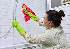 Una mujer limpia el espejo de un baño.