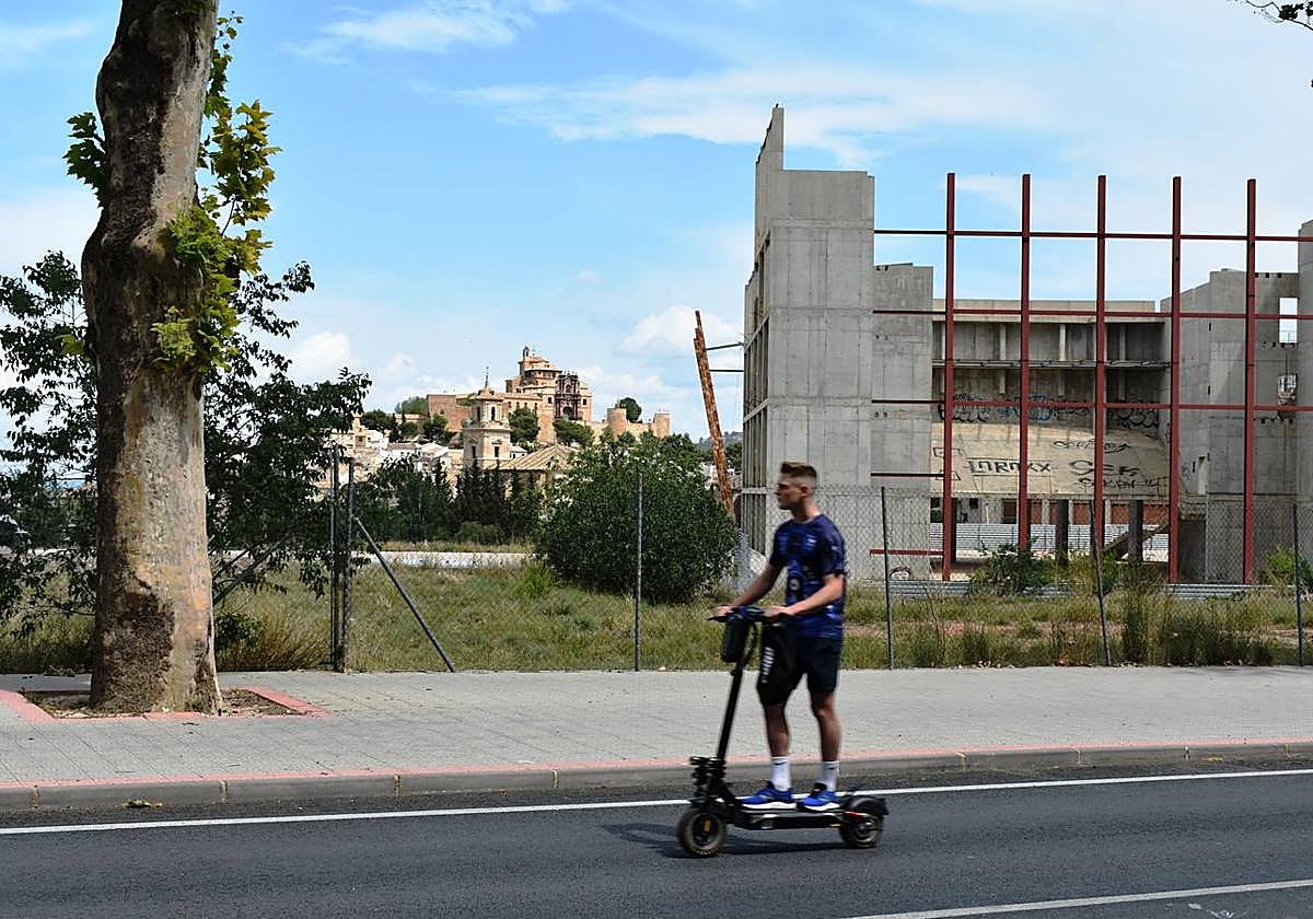 Un joven pasa con su patín eléctrico junto al edificio abandonado del auditorio, en Caravaca, cuyas obras se paralizaron hace diez años.
