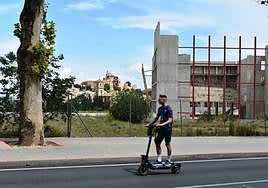 Un joven pasa con su patín eléctrico junto al edificio abandonado del auditorio, en Caravaca, cuyas obras se paralizaron hace diez años.