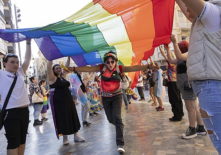 Una mujer pasa por debajo de la bandera LGTBIQ+, mientras otras personas la sujetan.