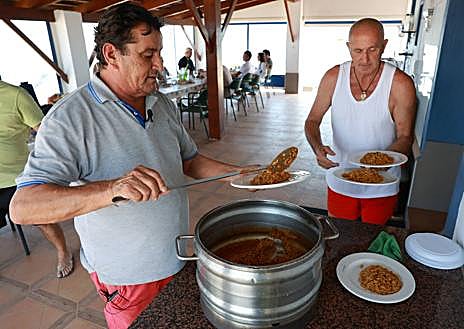 Imagen secundaria 1 - Muelle de acceso a la encañizada La Torre, solo para las embarcaciones privadas autorizadas; Julián Castejón y 'Sensi' sirven platos de caldero para los invitados; y una máquina draga el fango del fondo marino. 