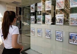 Una mujer observa el escaparate de una inmobiliaria con varias ofertas de pisos en venta, en una imagen de archivo.
