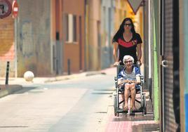 Una mujer traslada a una anciana, el pasado mes de julio, por una calle de Alcantarilla.