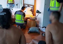 Dos detenidos observan cómo los agentes inspeccionan un dormitorio de la vivienda en la que se encontraban.
