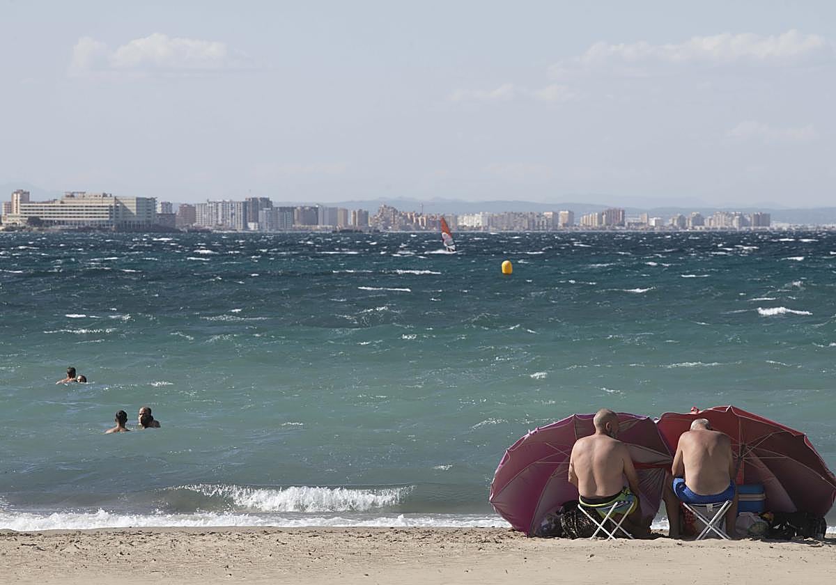 Dos bañistas se protegen con sus sombrillas del viento en una playa de Cabo de Palos.