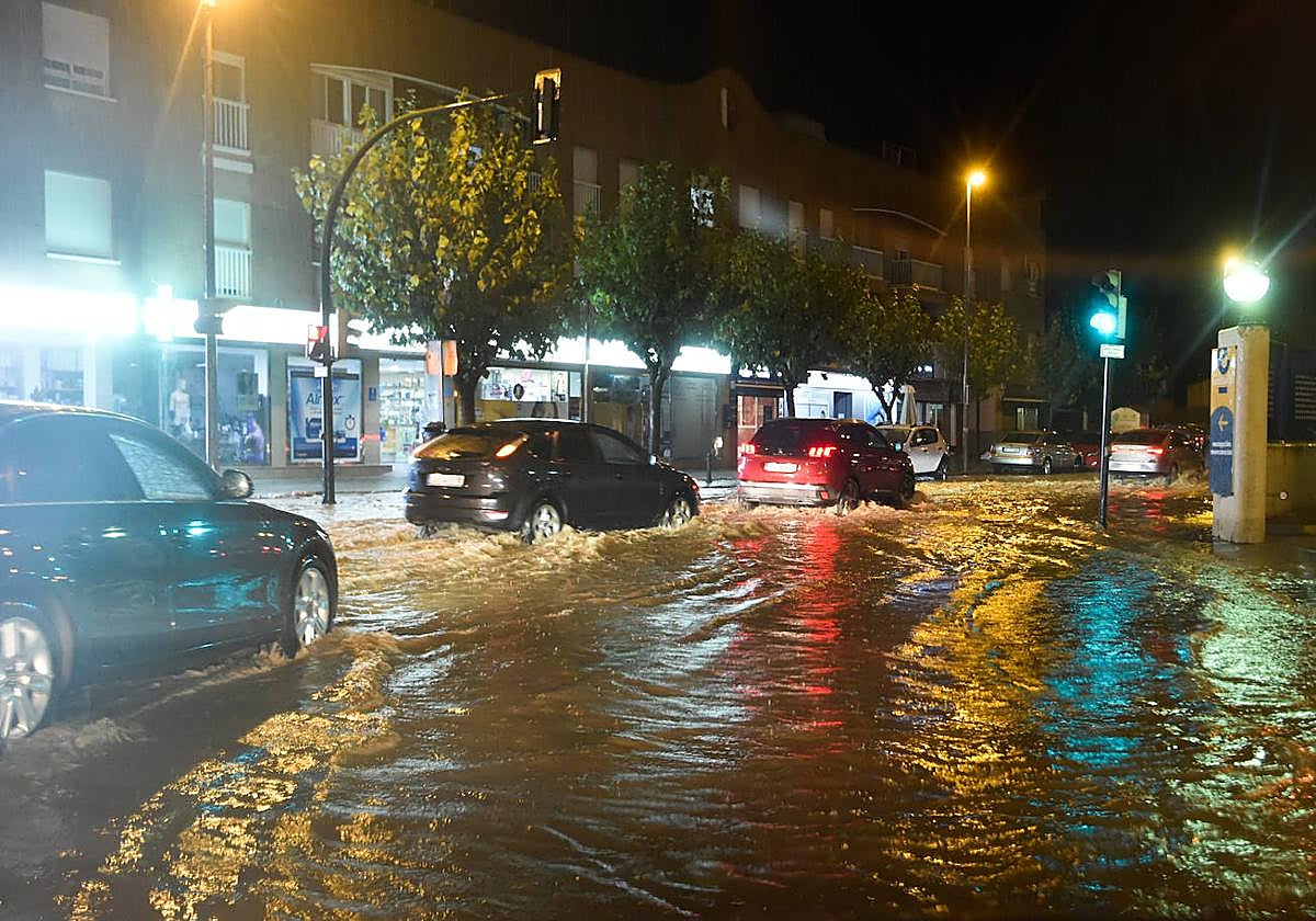 Vehículos circulando por una carretera inundada en la zona de la rambla de Churra.