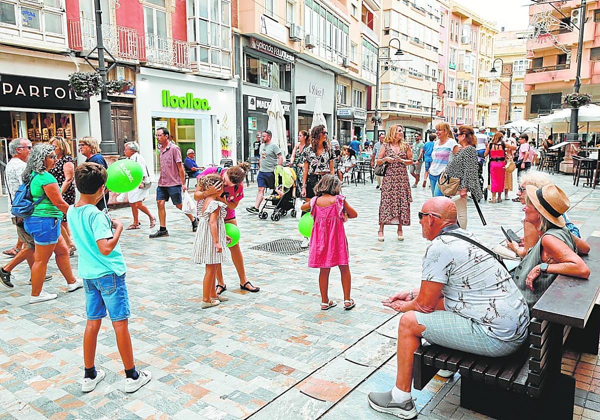 Decenas de personas pasean por la Puerta de Murcia el viernes festivo, junto a las terrazas de varios bares con mesas vacías.