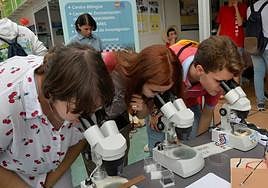 Tres personas observan objetos a través del microscopio en la Semana de la Ciencia de 2022.
