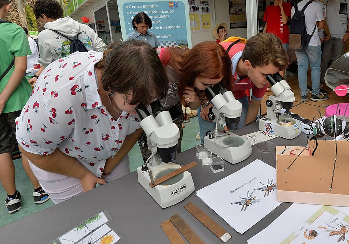 Tres personas observan objetos a través del microscopio en la Semana de la Ciencia de 2022.