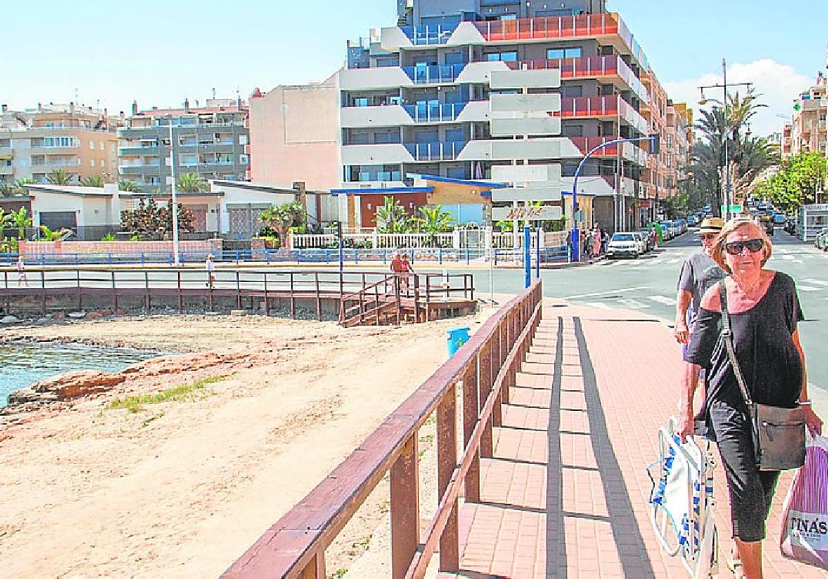 Bañistas pasean por la curva del Palangre. Al fondo, los terrenos donde se prevé edificar rascacielos.