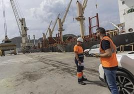 Dos trabajadores en los muelles de Escombreras, mientras otros descargan un barco de cereales.