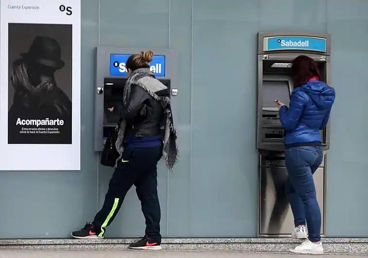 Dos mujeres consultan sus saldos antes de sacar dinero en cajeros, en una imagen de archivo.