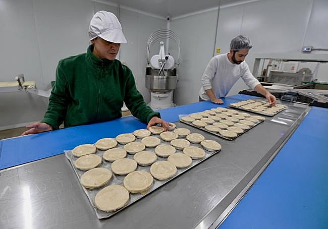 Dos trabajadores preparan pasteles de carne.