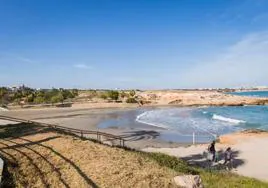 Dos turistas abandonan con sus sillas el arenal de Cala Mosca. Al fondo, todos los terrenos por construir hasta Punta Prima.