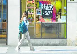 Una joven pasa junto al escaparate de un comercio de Murcia, con ofertas por el 'Black Friday'.