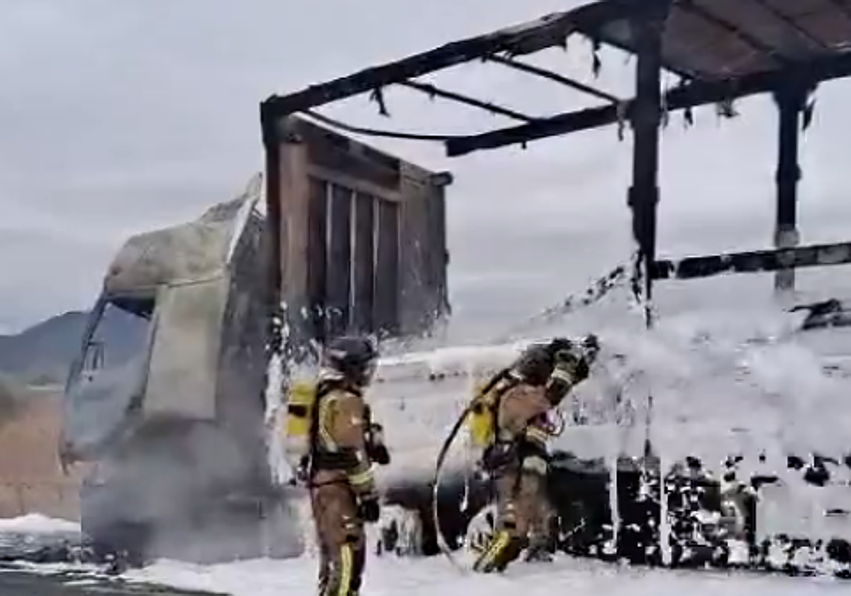 Dos bomberos apagan el fuego de un camión.